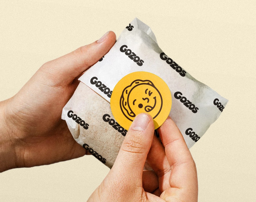Hands pressing a Gozos sticker onto a wrapped arepa