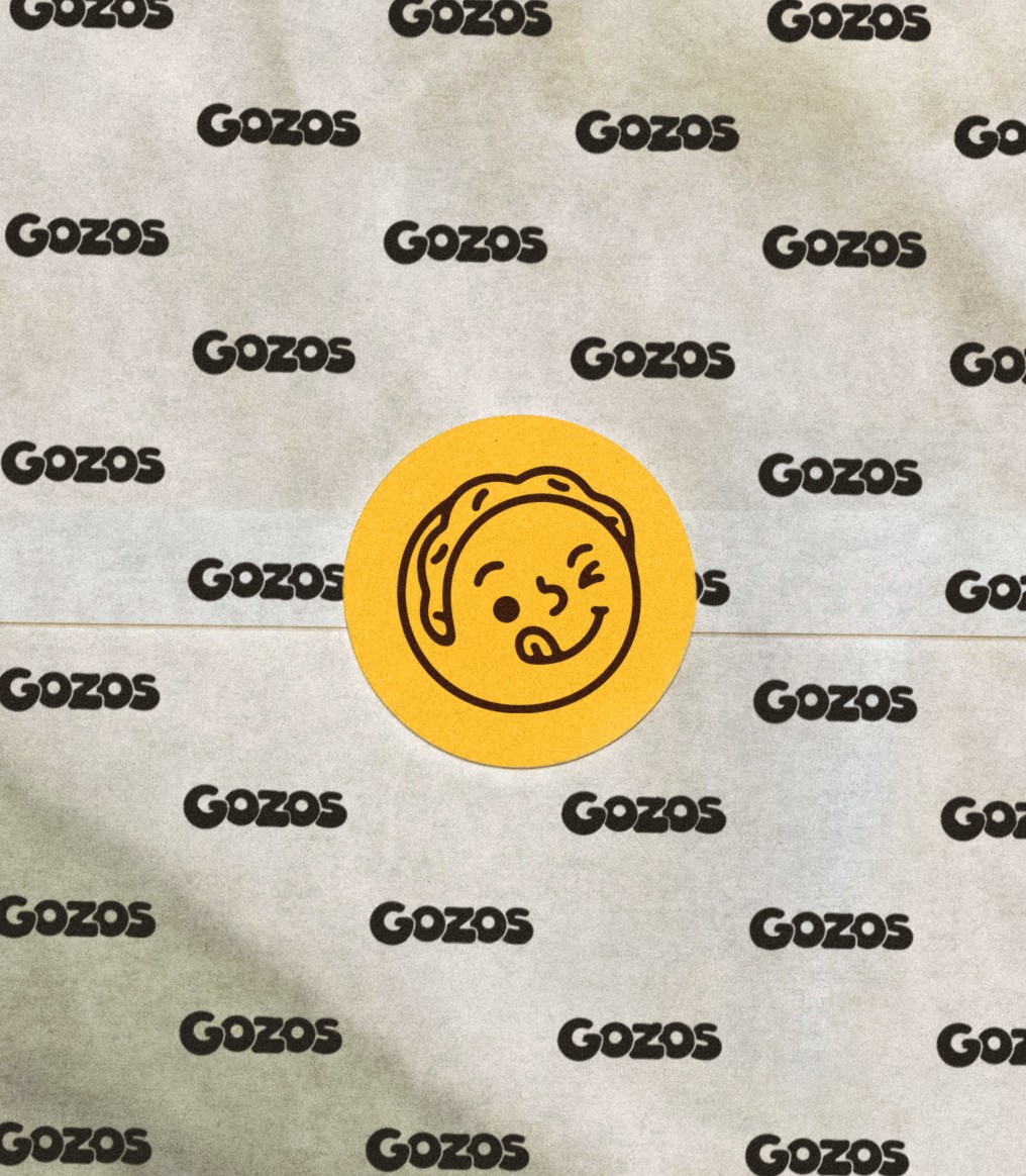 Gozos wrapping paper with the repeating wordmark, sealed with a mascot sticker