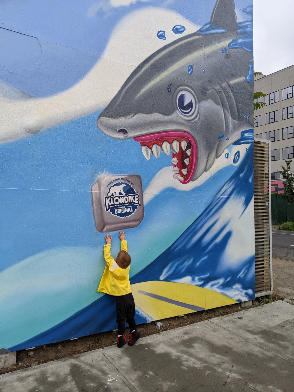 A child in a yellow raincoat stretching up for the Klondike bar in front of the shark