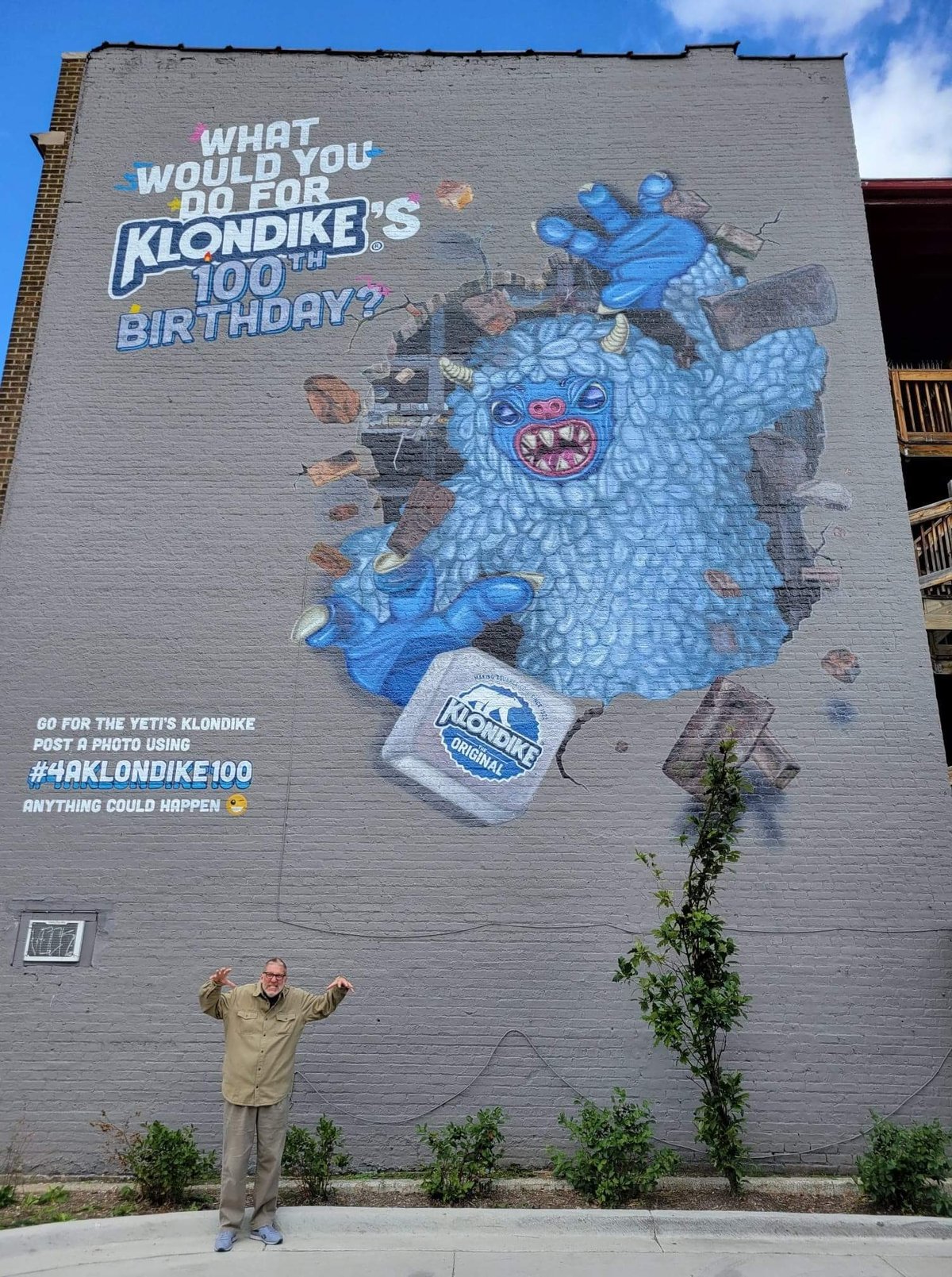 A visitor doing a monster pose beneath the Chicago yeti mural, which bursts out of a brick wall