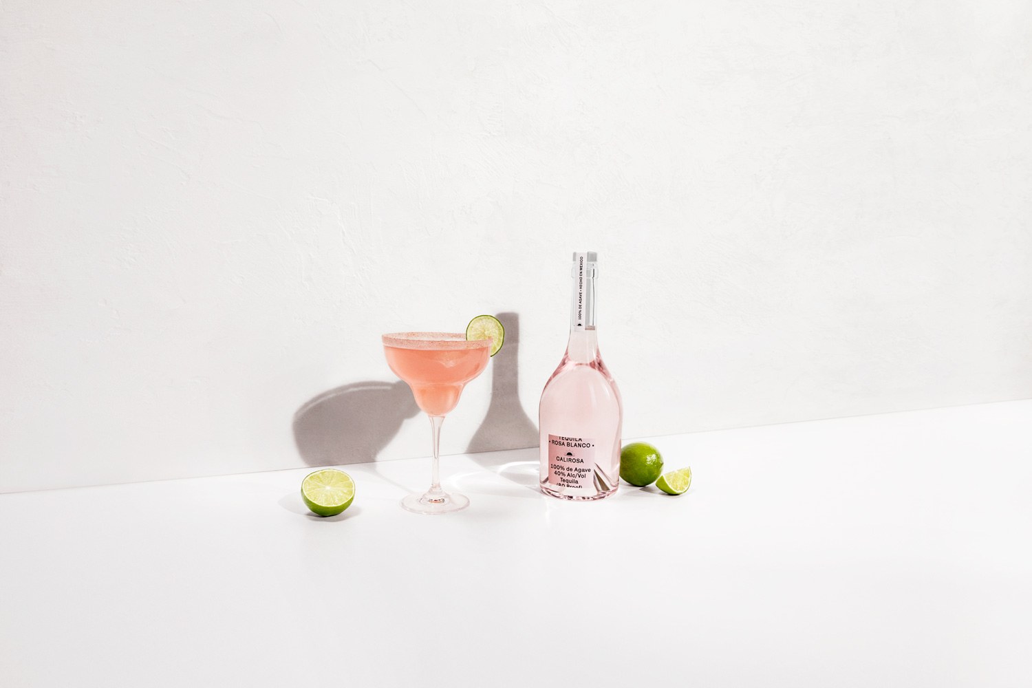 Rosa Blanco tequila bottle and cocktail with limes on white