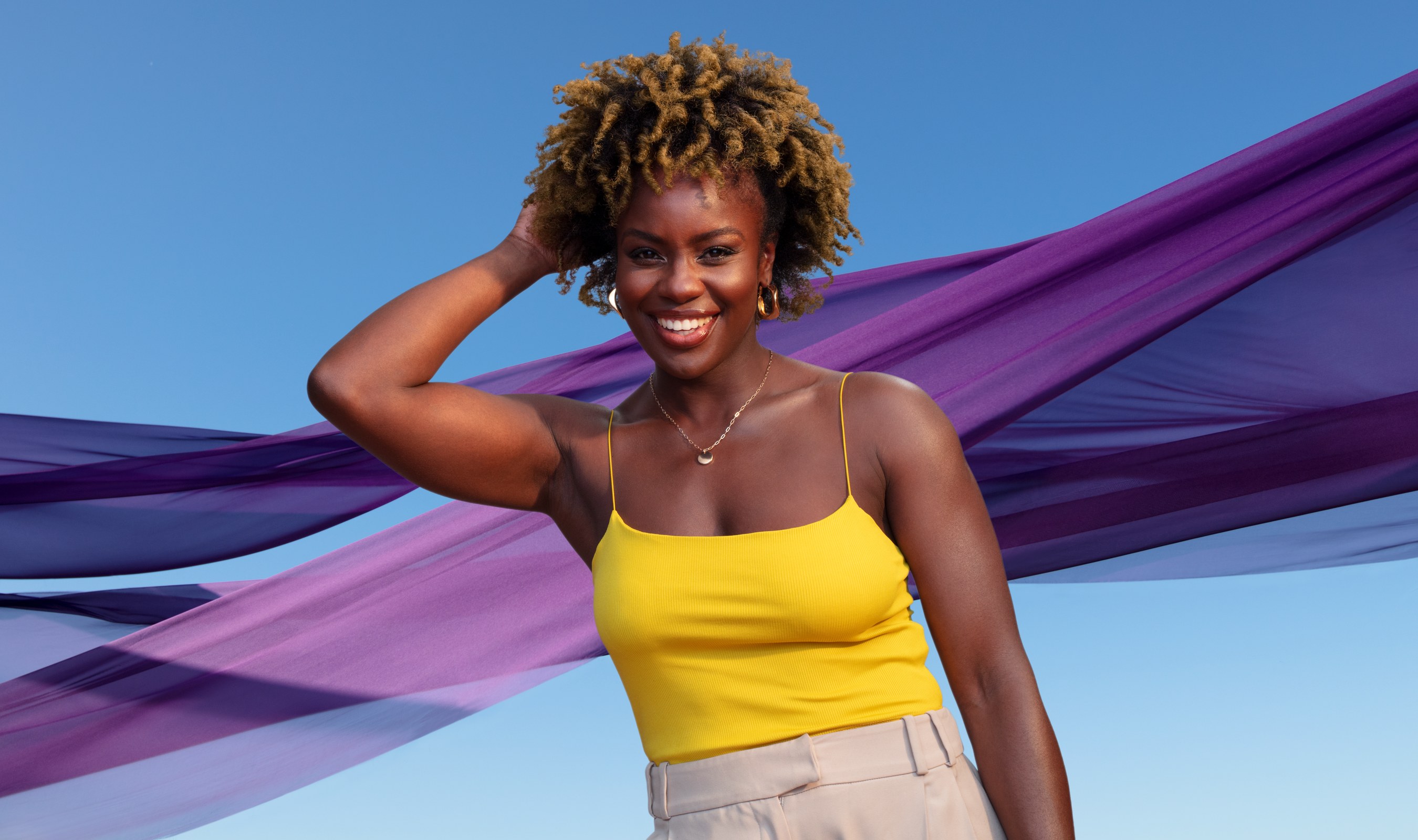 Schwarzkopf campaign: model in a yellow top with purple fabric against blue sky