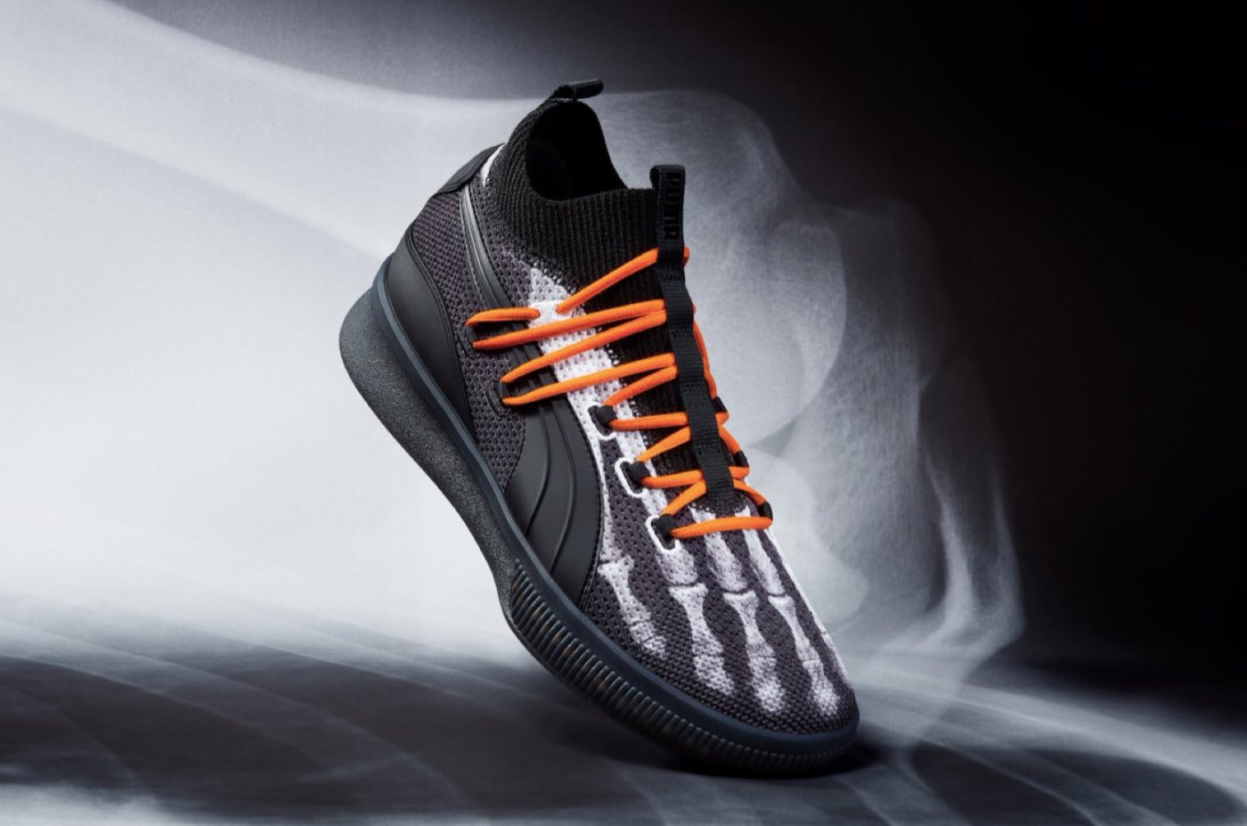 Sneaker with orange skeleton laces on a dark backdrop
