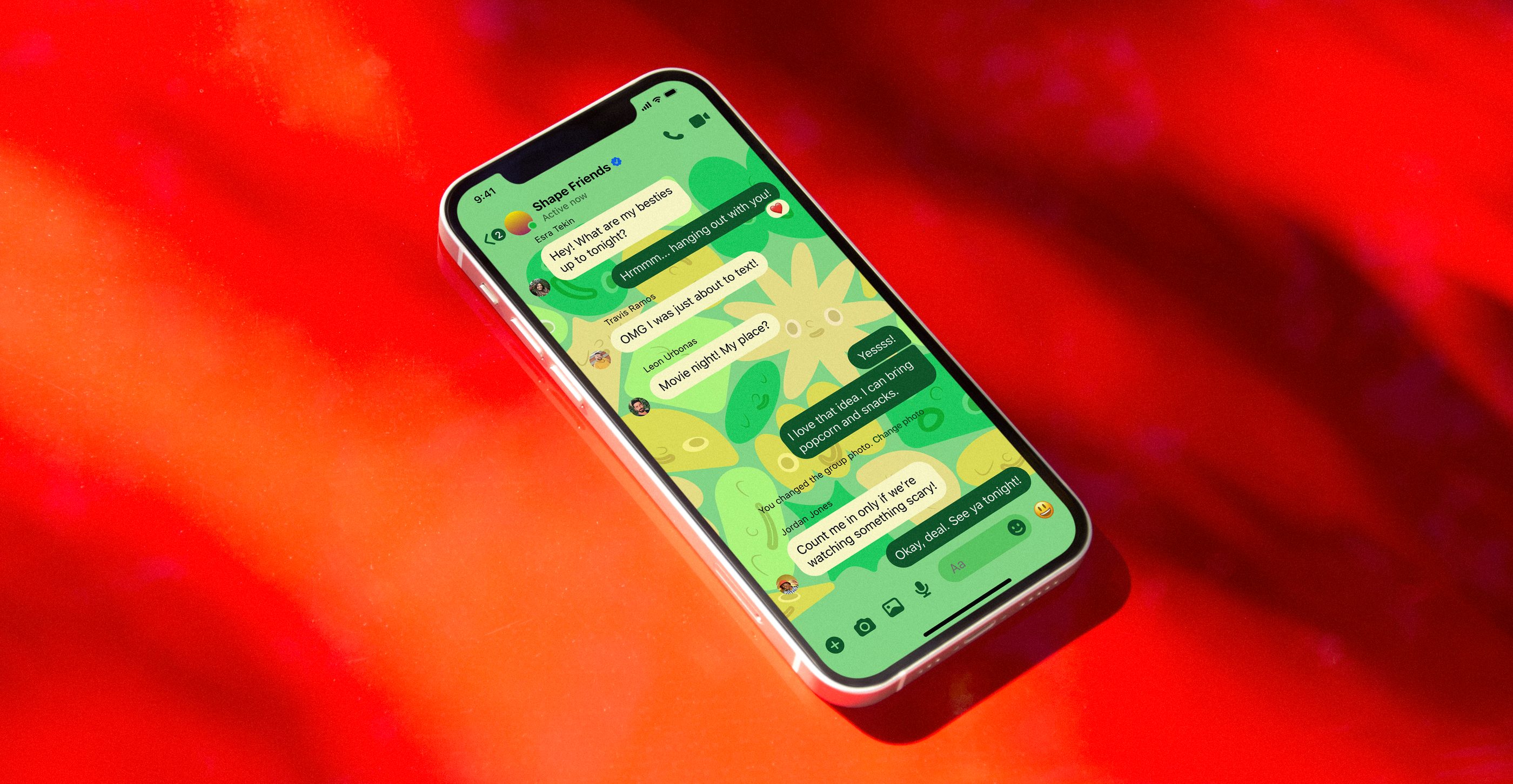 The Shape Friends theme in a Messenger group chat, on a phone resting on a red surface